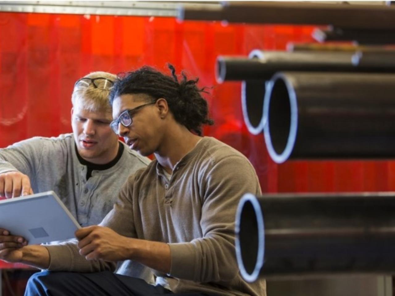 Two people looking at a laptop in a manufacturing facility.